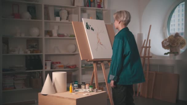 Una joven artista pintando ramas superiores de árbol en color verde en el estudio de arte - toma el color de la paleta — Vídeos de Stock