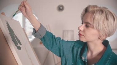 Sanat stüdyosunda kısa sarı saçlı, yeşil renkli genç bir kadın.