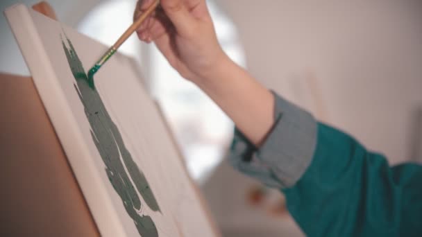 A young womans hand painting with a green color on the canvas in art studio — Stock Video