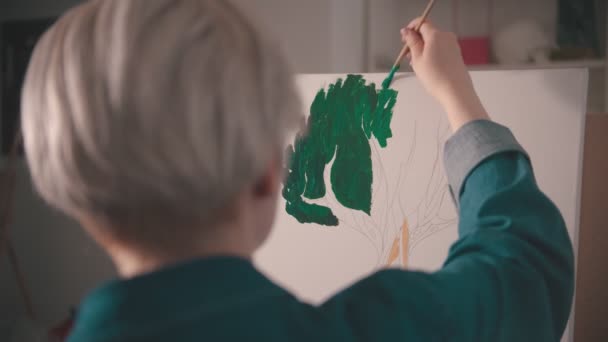 Μια νεαρή ξανθιά γυναίκα ζωγραφίζει με πράσινο χρώμα στον καμβά — Αρχείο Βίντεο