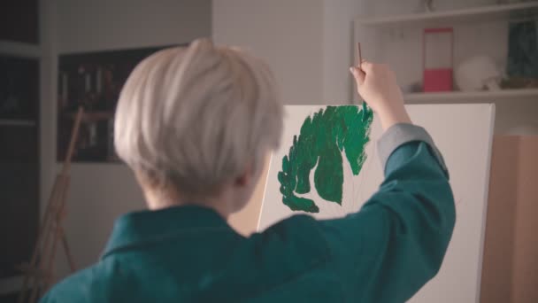 Молодая женщина с короткими волосами раскрашивает верхние ветви дерева зеленым цветом в художественной студии — стоковое видео