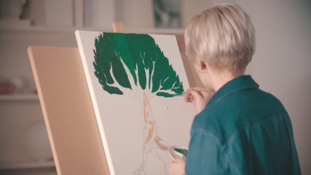Молода блондинка малює картину з зеленим кольором на полотні — стокове відео