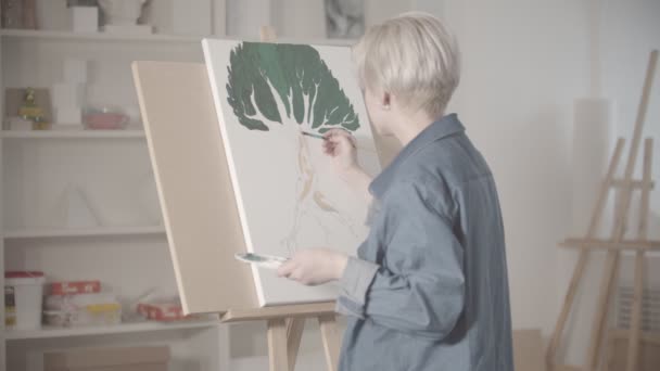 A young blonde woman draws a tree with paints — Stock Video