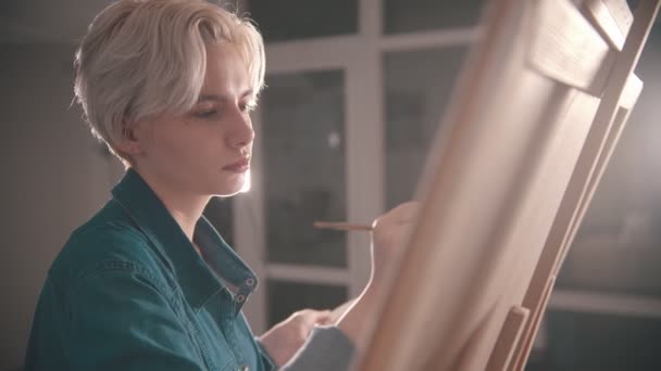 若いブロンドの魅力的な女性アーティストがアートスタジオで絵を描く — ストック動画