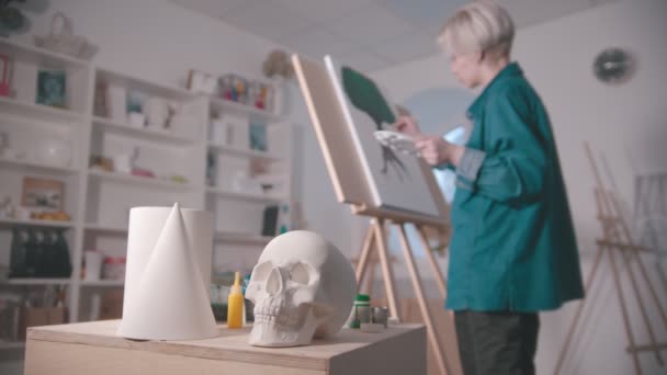 Молода жінка-художник в художній студії череп та інші фігури на столі — стокове відео