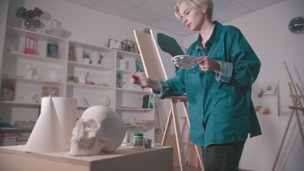 Mladá žena malířka v ateliéru umění - lebka a další postavy na stole — Stock video