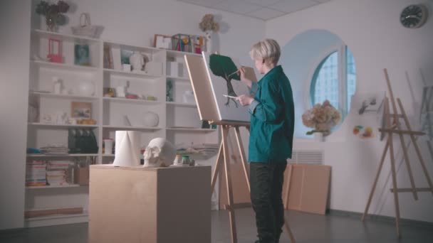 Egy fiatal nő művész a művészeti stúdióban - csinál egy fa festmény - egy koponya és más figurák az asztalon — Stock videók