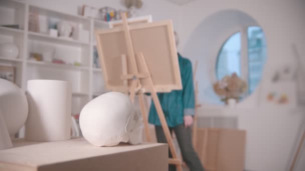 A young woman with short blonde hair drawing a skull and other figures from the table — Stock Video