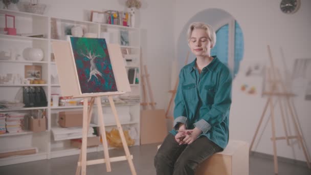 ศิลปินหญิงสาวนั่งอยู่ในสตูดิโอศิลปะหลังจากเสร็จสิ้นการวาดภาพ — วีดีโอสต็อก
