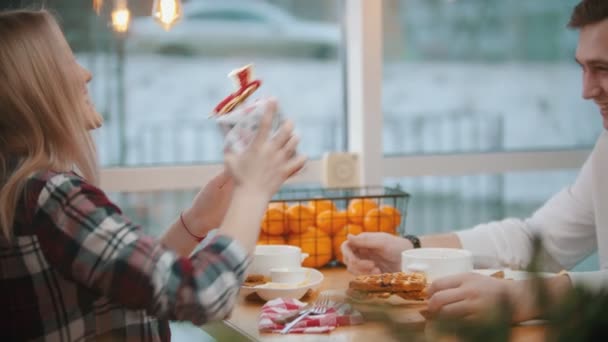 Ett par på caféet - en kvinna ger sin pojkvän en gåva - en man kysser henne på kinden — Stockvideo