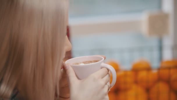 Młoda kobieta z jasnymi włosami pijąca kawę z pianką — Wideo stockowe