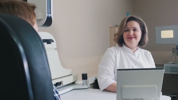 Лікування офтальмолога - усміхнена жінка-лікар, яка перевіряє зір хлопчиків — стокове відео