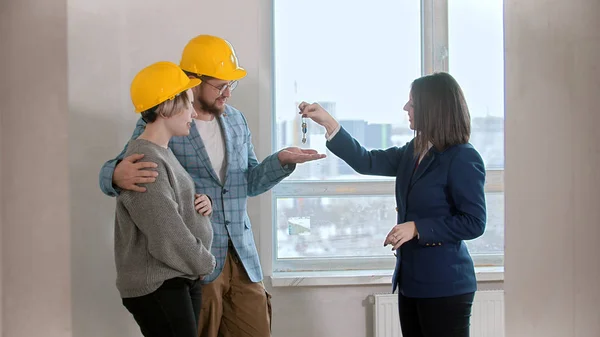 Een makelaar geeft de sleutels van het appartement aan een jong gezin — Stockfoto