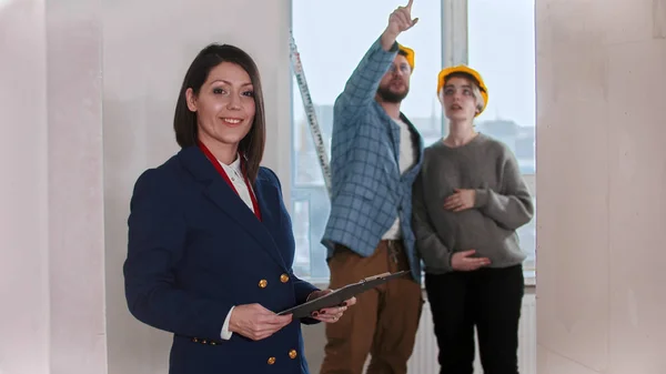 Een glimlachende makelaar in het ontwerp appartement - jong getrouwd stel op de achtergrond — Stockfoto