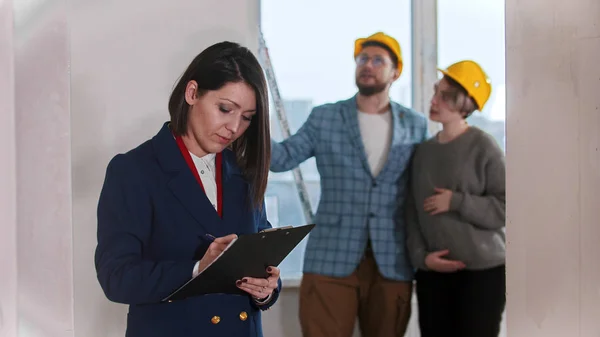 Een makelaar die papieren ondertekent - jong getrouwd stel op de achtergrond — Stockfoto