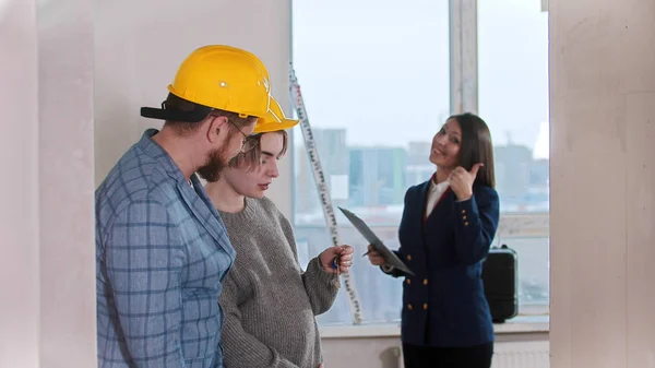 Een zwangere vrouw met haar man die naar de sleutels kijkt vanuit een nieuw appartement - een makelaar die een duim omhoog laat zien — Stockfoto