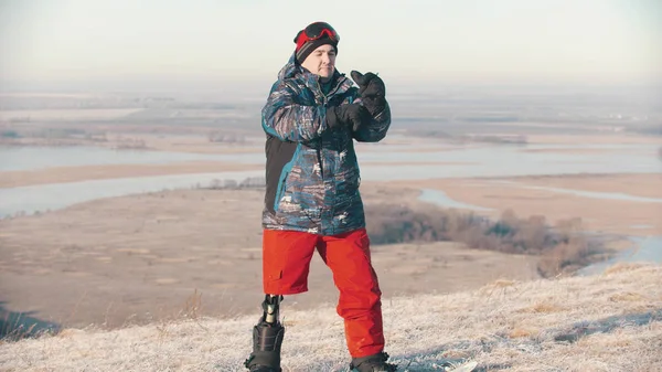 Snowboarding - A man with prosthetic leg standing on the board and putting on protective gloves — 스톡 사진