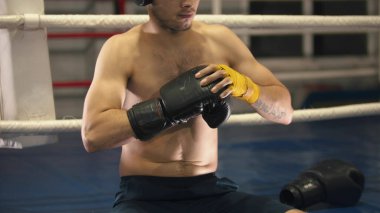 A man boxer sitting on the ring with one boxer glove on