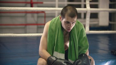 A tired man boxer sitting on the ring with green towel on his shoulders