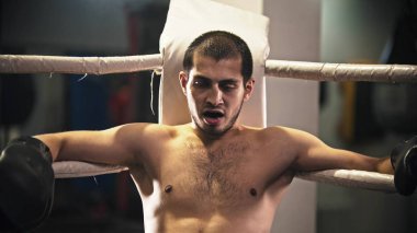 Köşede ağzında diş koruyucusuyla ringde oturan yorgun bir boksör.