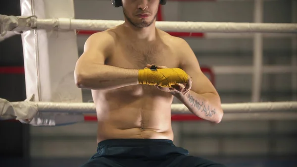 Ein müder Boxer mit Kopfhörern, der seine Hände auf dem Ring bandagiert — Stockfoto