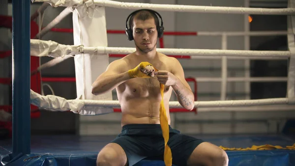 Kulaklıklı bir boksör ellerini bandajlıyor ve ringde oturuyor. — Stok fotoğraf