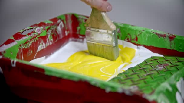 Змішування біло-жовтих кольорів у лотку фарби за допомогою синтетичного пензля — стокове відео