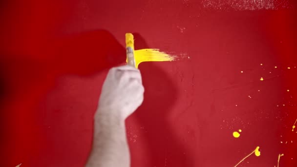 Una persona pintando una casa con una pintura amarilla en la pared roja — Vídeos de Stock