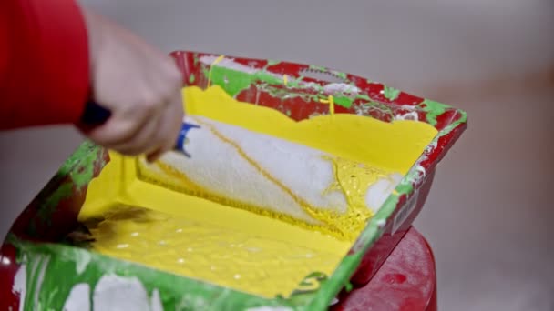 A person covering a roller in yellow paint in the paint tray — 비디오