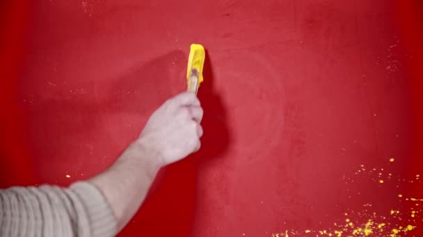 Uma pessoa pintando um rosto sorridente com uma tinta amarela brilhante na parede vermelha — Vídeo de Stock