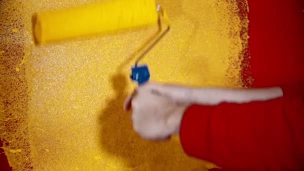 Een persoon die een rode muur schildert met gele verf met behulp van een roller — Stockvideo
