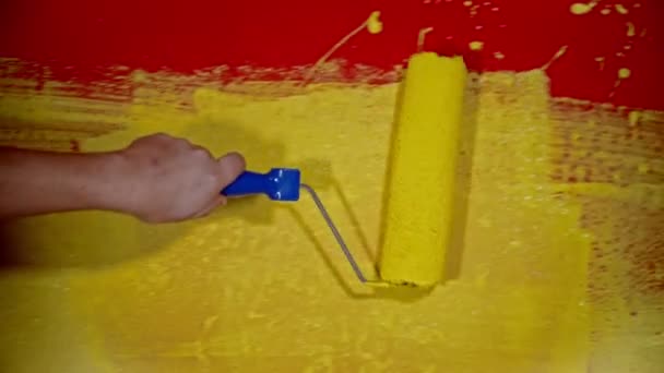 La reparación del apartamento - la persona que pinta la pared roja con la pintura amarilla usando el rodillo — Vídeos de Stock