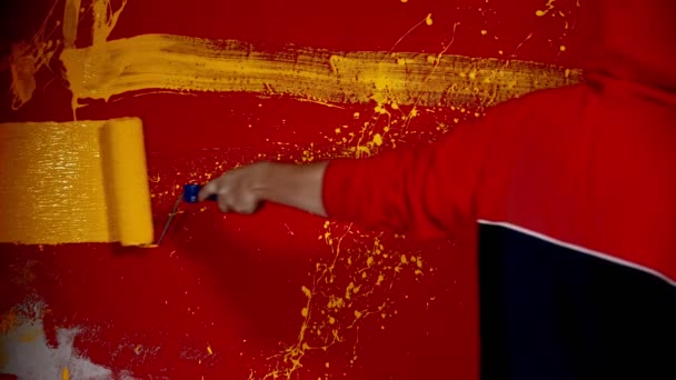 Un hombre caminando por la pared roja y pintando líneas con un color amarillo usando un rodillo — Vídeos de Stock