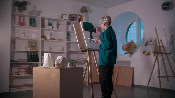 Uma jovem artista no estúdio de arte - fazendo uma pintura em árvore - um crânio e outras figuras na mesa — Fotografia de Stock