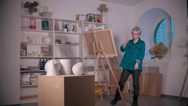 Una joven artista atractiva dibujando un cráneo y otras figuras de la mesa —  Fotos de Stock