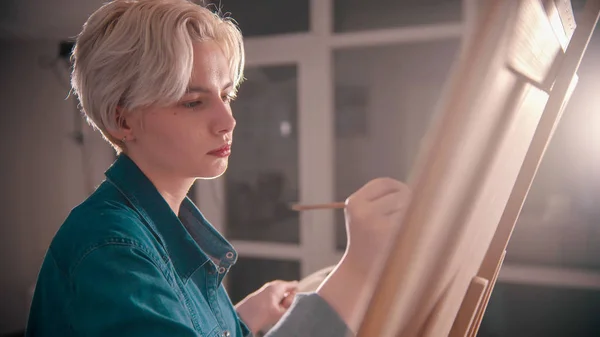Una joven rubia atractiva artista dibuja una pintura en el estudio de arte —  Fotos de Stock