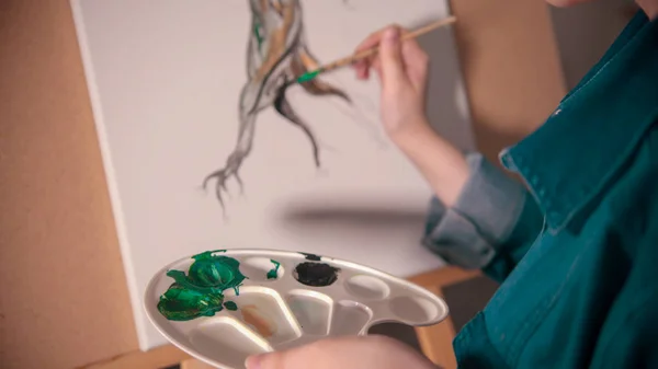 A young woman artist painting tree trunk in darker color — 스톡 사진