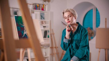 Resmini bitirdikten sonra sanat stüdyosunda oturan genç bir kadın sanatçı.