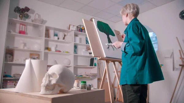 A young blonde woman draws a tree with paints in the art studio — 스톡 사진