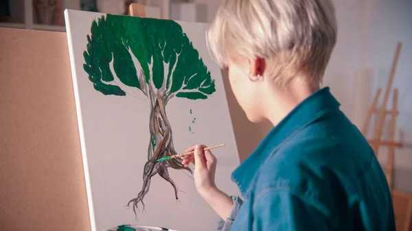 Młoda blondynka rysuje drzewo z farbami w studiu — Zdjęcie stockowe