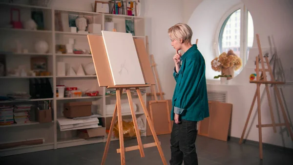 A young woman sketching an abstract tree on the canvas and looking at it — 스톡 사진