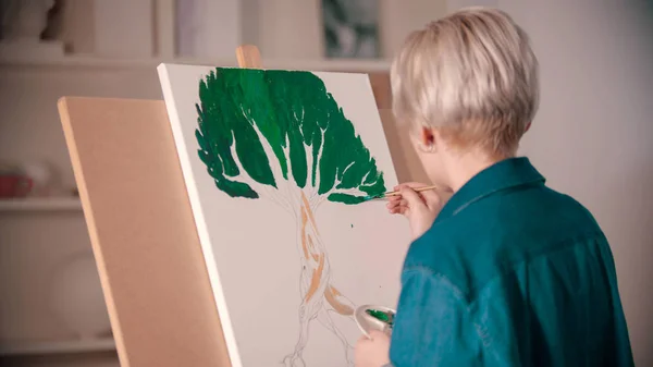 A young blonde woman draws a tree using paints — 스톡 사진