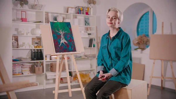 A young woman artist with short blonde hair sitting in the art studio