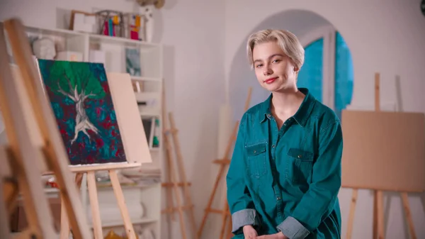 Una joven artista sonriente con el pelo corto y rubio sentado en el estudio de arte —  Fotos de Stock