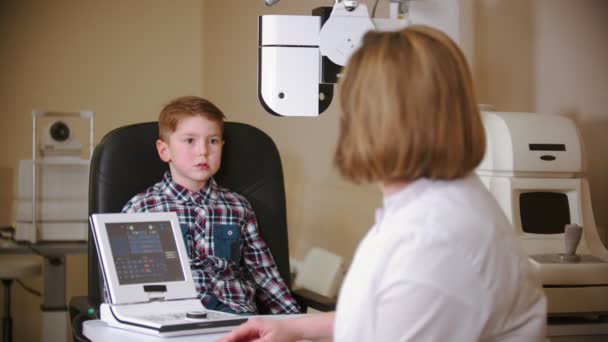 Een behandeling in oogkliniek - het controleren van kleine jongens oog visie door te kijken door middel van grote speciale apparaat — Stockvideo