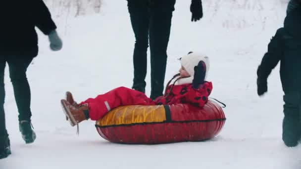 Familie rennen en spelen buiten in de buurt van het bos - man rolt zijn dochter op de opblaasbare slee — Stockvideo