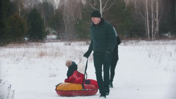 Familia corriendo y jugando al aire libre cerca del bosque - hombre rueda a sus hijos en el trineo inflable — Vídeos de Stock