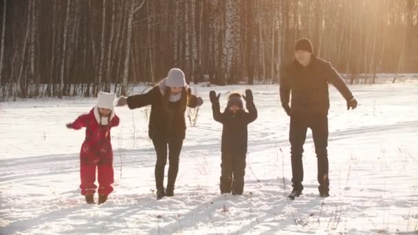 Una famiglia felice che si tiene per mano e salta vicino alla foresta invernale al tramonto — Video Stock