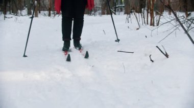 A woman trying to ski in the woods - stop moving and unsetting her boots from the ski
