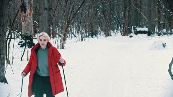 Una joven rubia caminando sobre el esquí en el bosque y mirando alrededor — Vídeos de Stock